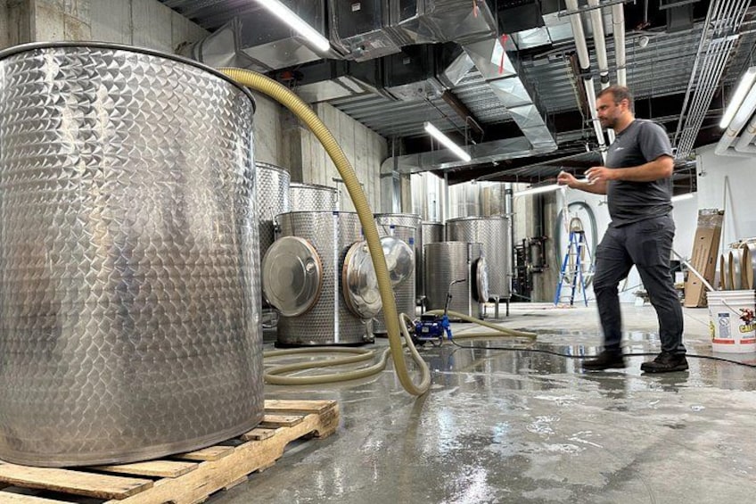 A person in a brewery setting with stainless steel tanks and hoses. 4