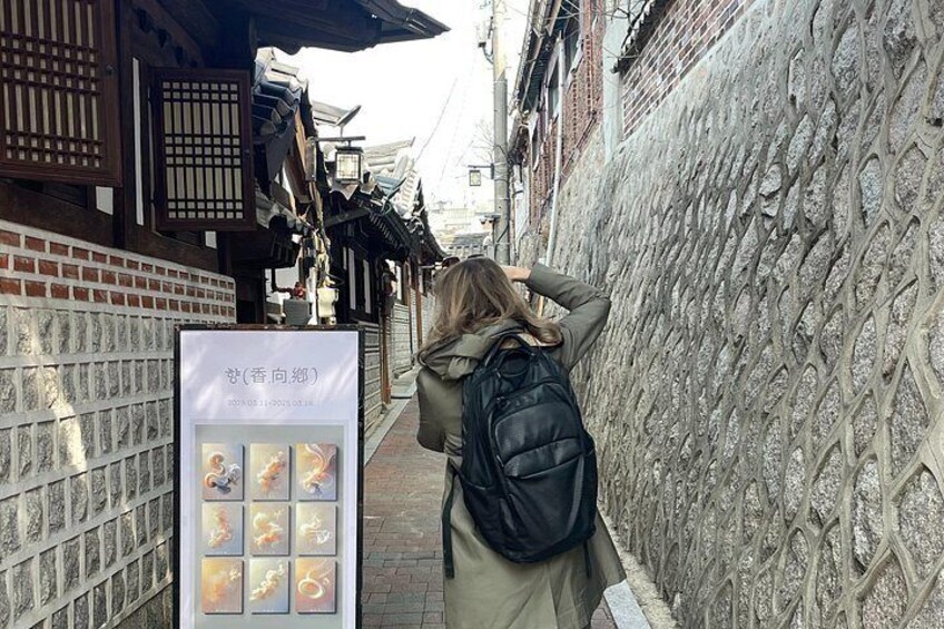 A person with a backpack standing in front of a traditional building with a stone wall. 5