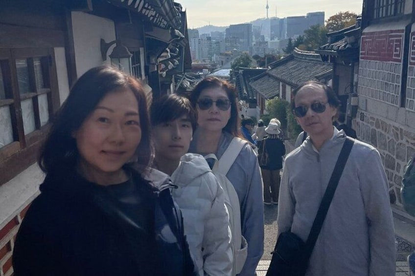 A group of people standing on a street with traditional architecture and a modern cityscape in the background. 2