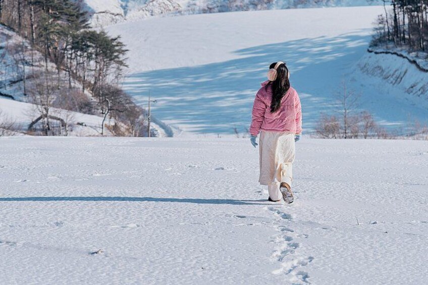 A person walking on a snow-covered path with a frozen lake and trees in the background. 3
