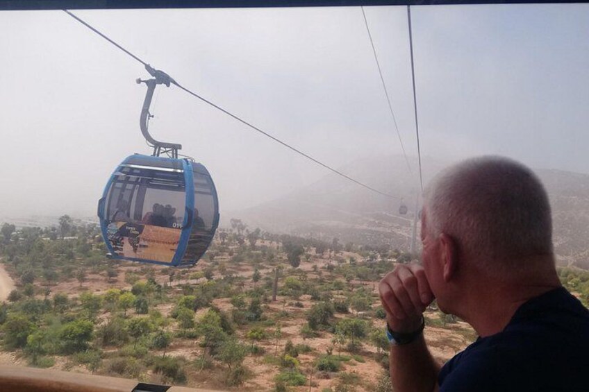 A cable car in motion, a person observing, and a landscape with sparse vegetation. 3