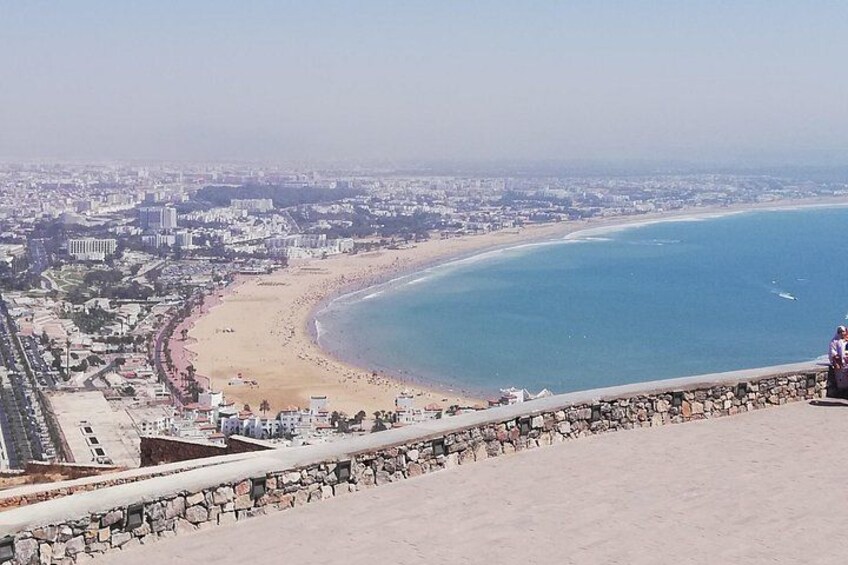 A coastal cityscape with a beach, a stone wall, and a distant city skyline. 2