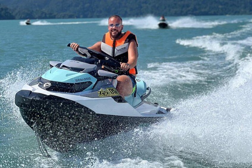 En person kører på en jetski på vandet med bølger, og en anden båd ses i baggrunden. 2