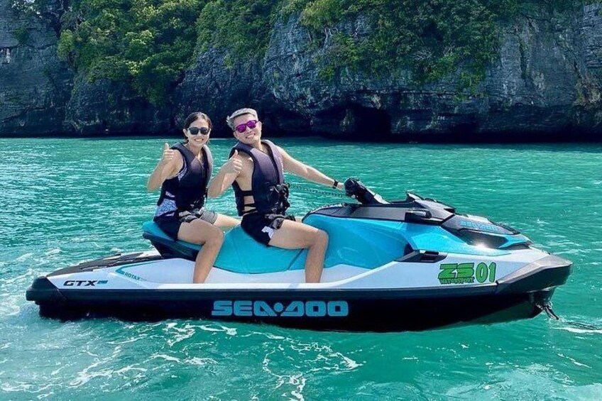 Two people on a Sea-Doo jet ski with a rocky coastline in the background. 2