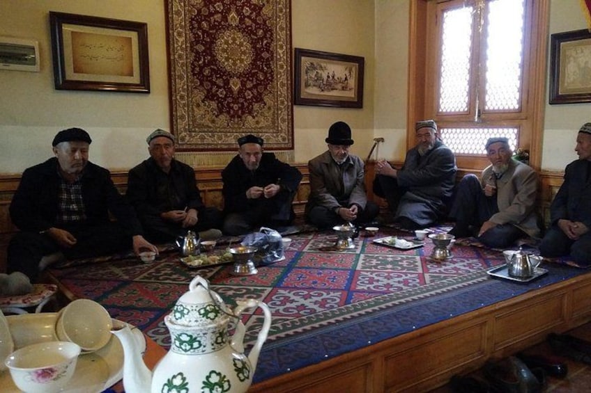 A group of men seated around a table with traditional tea sets and a patterned carpet. 2