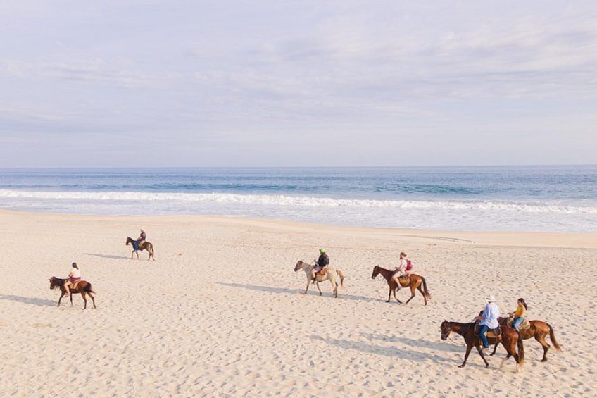 A beach with people riding horses. 1