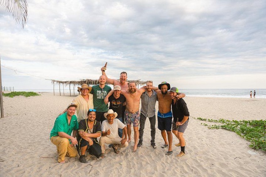 A group of people on a sandy beach with a thatched structure in the background. 3
