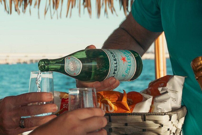 A person pouring a beverage into a glass, with a basket of snacks and a bottle labeled 'Pellegrino' in the foreground. 2