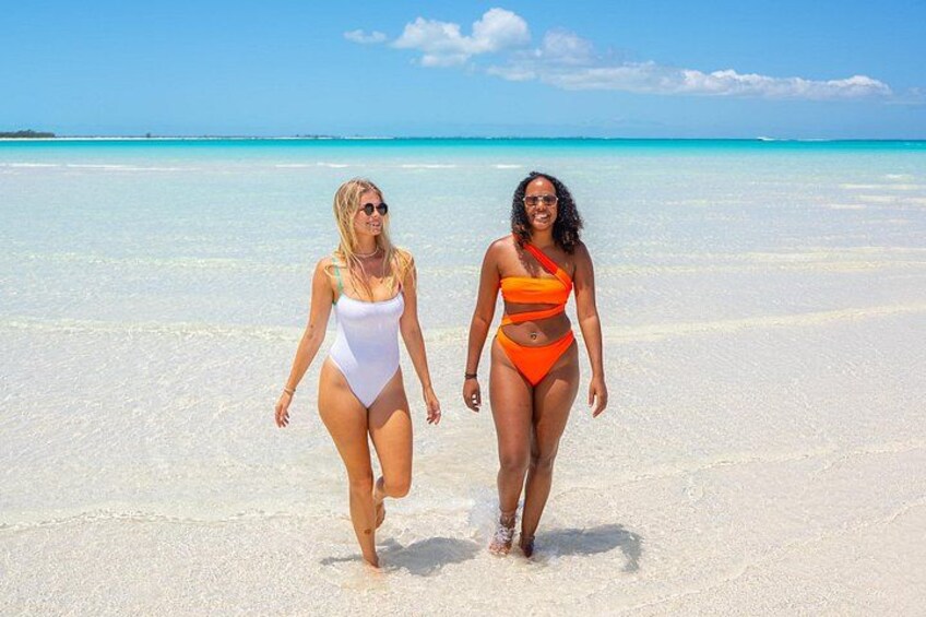 Dos personas caminando sobre una playa arenosa con agua turquesa cristalina al fondo. 4