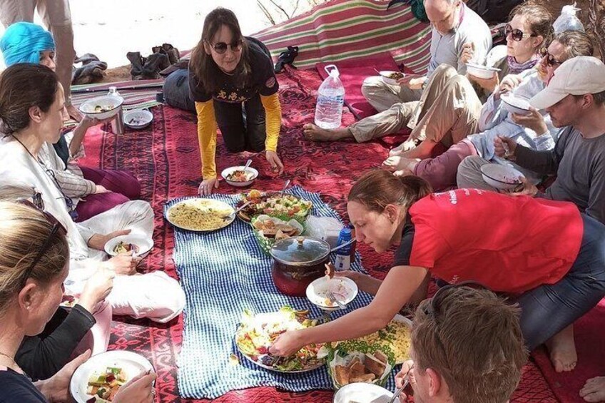 A group of people sitting on a red carpeted area, eating from plates and bowls. 2