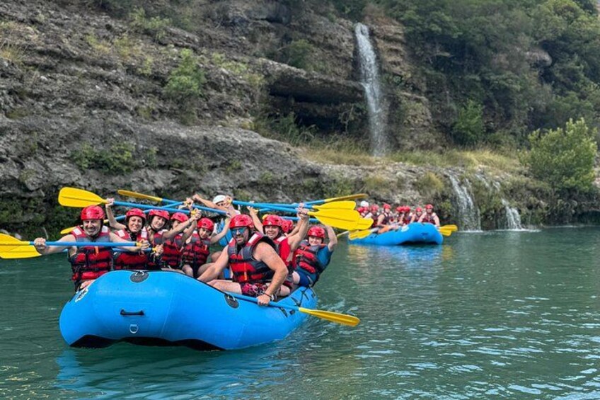 A group of people in a blue raft on a river, paddling with yellow paddles. 3