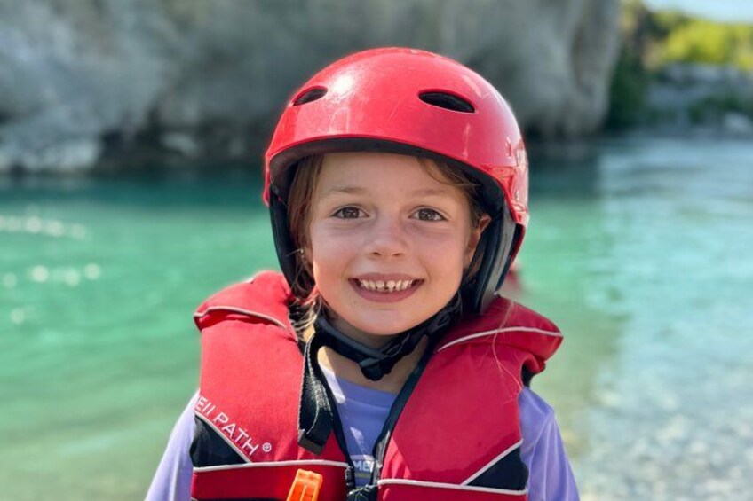 Een persoon met een rode helm en een reddingsvest staat bij een waterlichaam met een rotsachtige achtergrond. 3