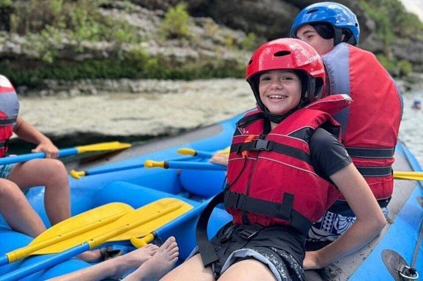 People in a blue raft wearing red life jackets and helmets. 4