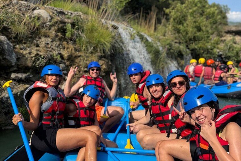 A group of people in a blue raft on a river, wearing life jackets and helmets. 5