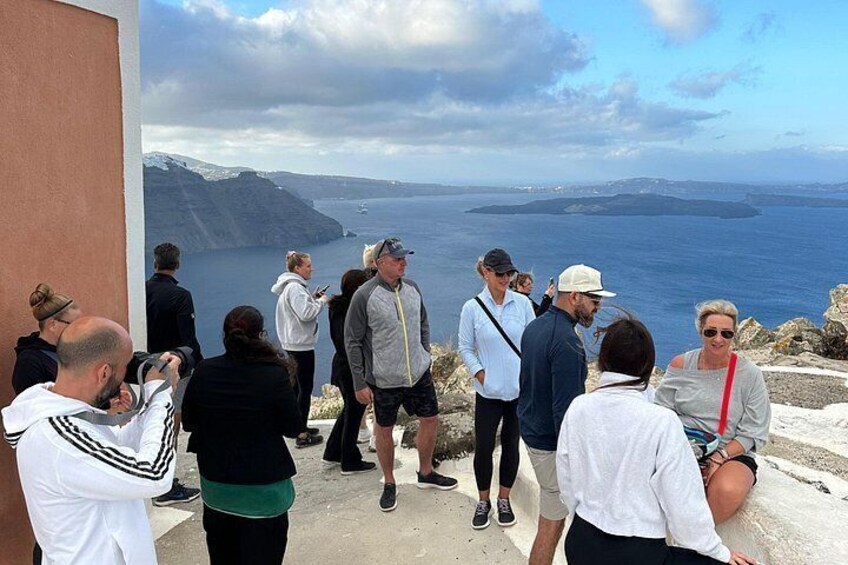 En gruppe mennesker står ved en klippe med udsigt over havet, med stengrund og en klar himmel. 3