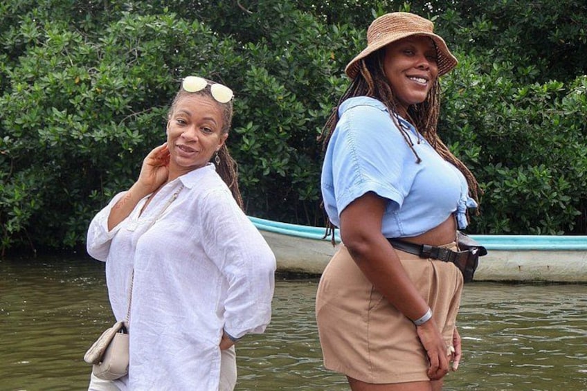 Dos mujeres están junto al agua, con abundante vegetación al fondo. 4