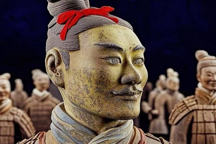 A terracotta statue with a red ribbon, surrounded by similar statues. 2