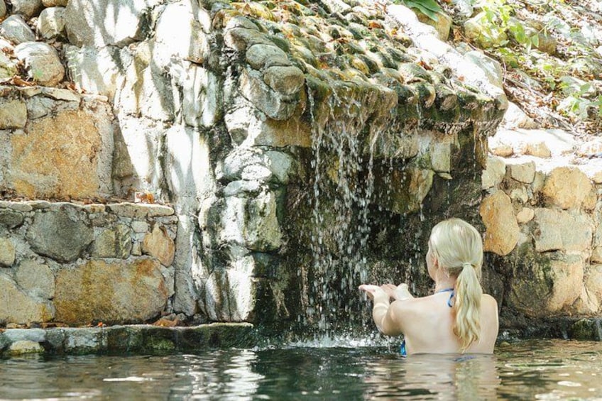Une personne se trouve dans une piscine naturelle, bordée d’un mur de pierres et agrémentée d’une cascade. 5