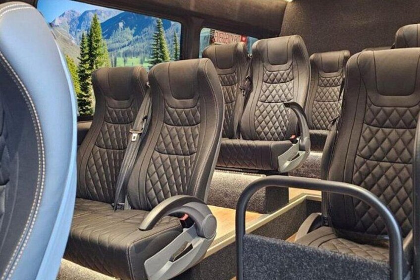 A vehicle interior with four black leather seats, a steering wheel, and a gear shift. 4