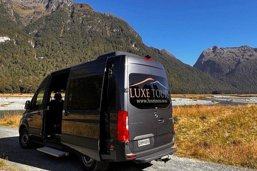 A black van with 'LUXE TOURS' branding parked on a road with a mountainous backdrop. 2