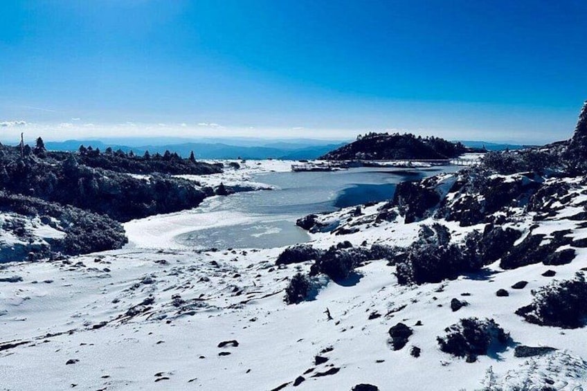 A snow-covered landscape with a frozen lake, rocky terrain, and distant hills. 2