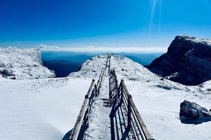 A snow-covered mountain path with wooden railings, leading to a distant view of the horizon. 3