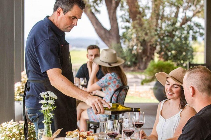A waiter serving wine to guests at an outdoor dining table. 3