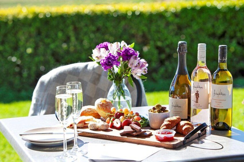 A picnic setup with a table, wine bottles, a vase of flowers, and food. 1
