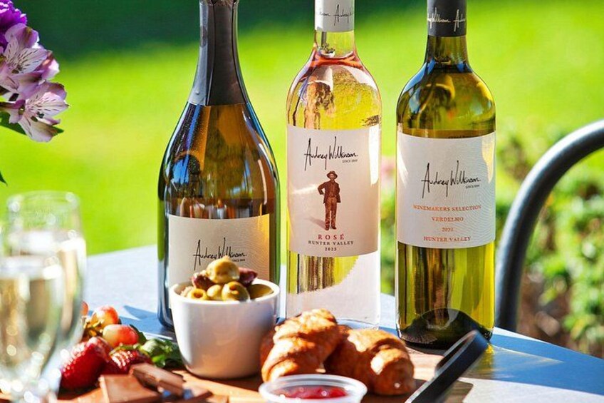 Three bottles of wine, a bowl of nuts, and a plate of pastries on a table outdoors. 5