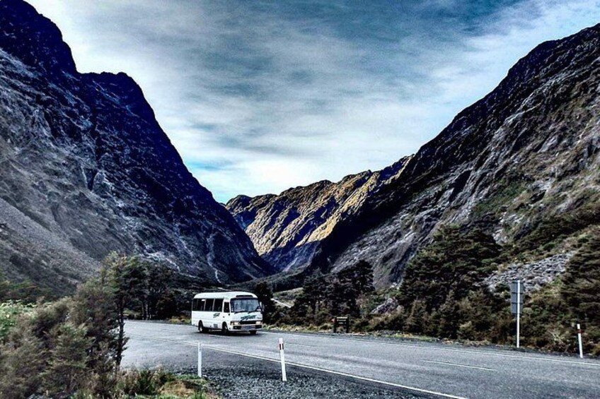 A white van driving on a road flanked by steep, rocky mountains. 4