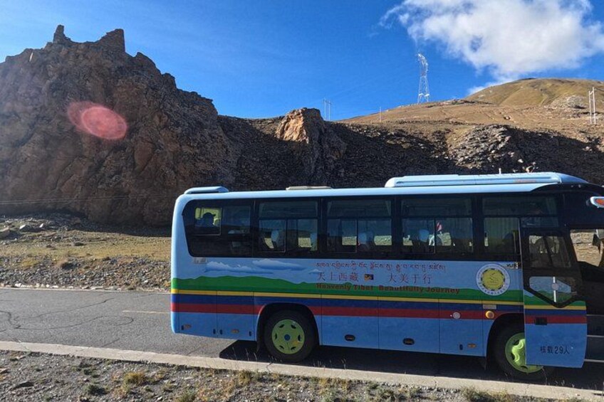A bus with a colorful design, parked on a road with a rocky mountain and a transmission tower in the background. 3
