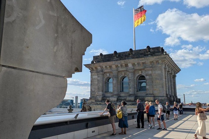 Un edificio histórico con una bandera, gente reunida y una estructura moderna al frente. 2