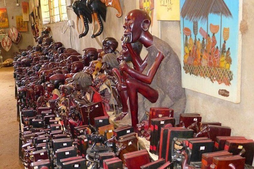 A collection of wooden sculptures and masks, some with animal heads, displayed in a shop with a large painting on the wall. 5