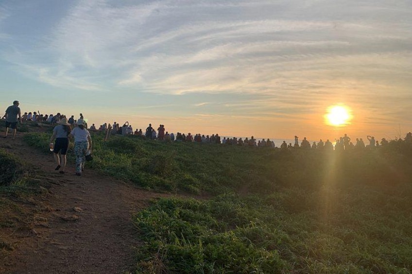 Un atardecer sobre una colina cubierta de hierba, con gente caminando y sentada. 2