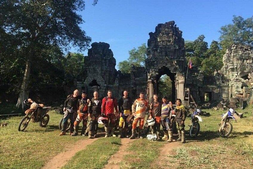 A group of people posing in front of ancient ruins with a motorcycle in the background. 4