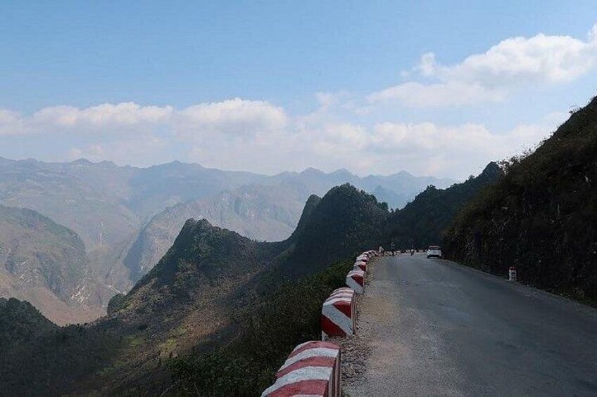 A winding mountain road with guardrails, surrounded by steep hills and a clear sky. 3