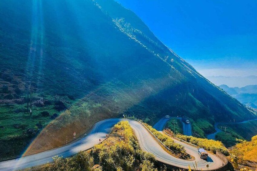A winding mountain road with a vehicle, surrounded by lush greenery and a clear blue sky. 4