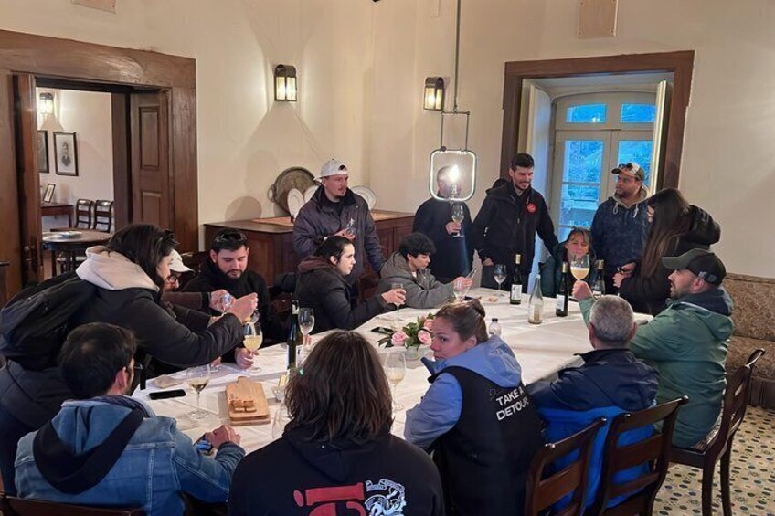 Eine Gruppe von Personen sitzt an einem Tisch in einem Raum, der von einem Kronleuchter und einer Tür im Hintergrund geschmückt ist. 2