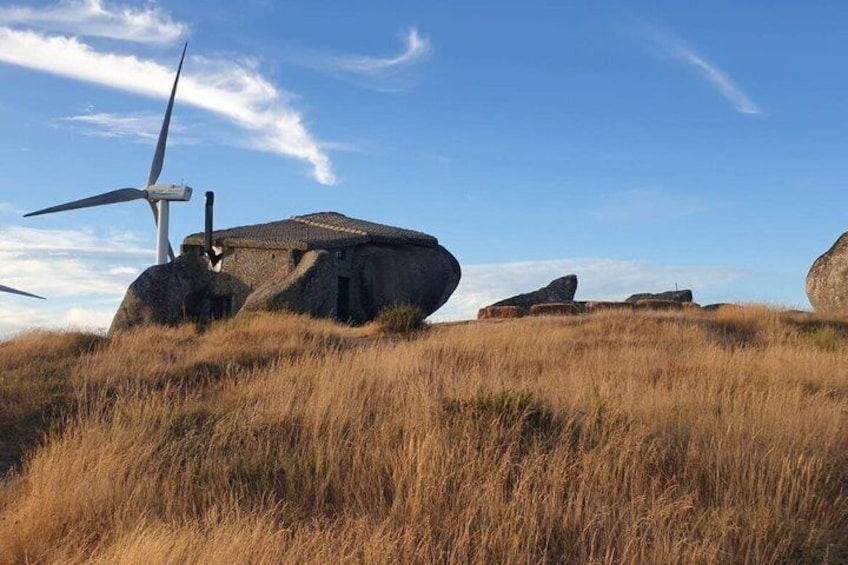 Eine Windkraftanlage, ein Steinbauwerk und ein grasbewachsenes Feld unter blauem Himmel. 4