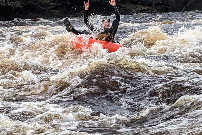 Een persoon in een neopreenpak die op een rode vlot door woelig water vaart. 2