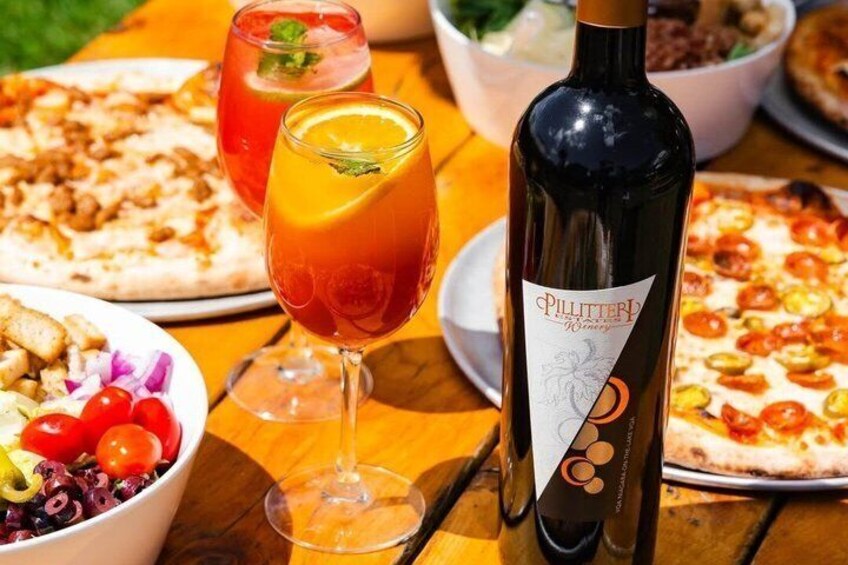 Una mesa con diversos alimentos, entre ellos pizzas y una ensalada, junto con dos vasos de una bebida roja. 5