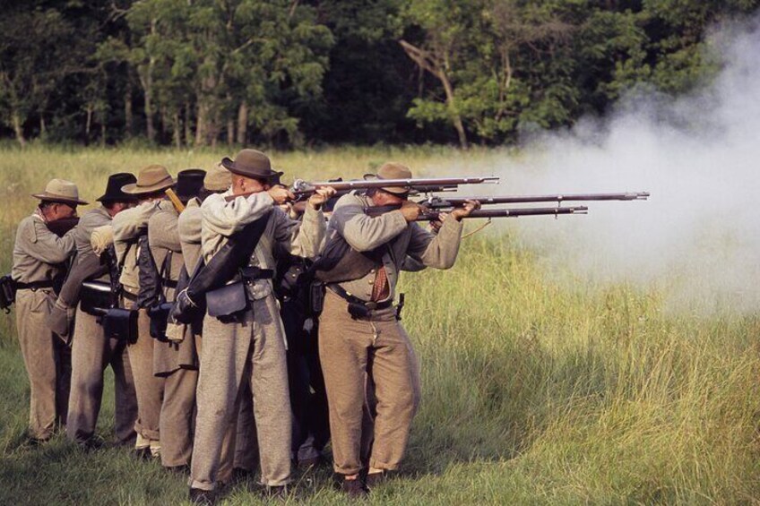 Un grupo de hombres con uniformes de campo apuntando rifles en un campo cubierto de hierba, con árboles al fondo. 5