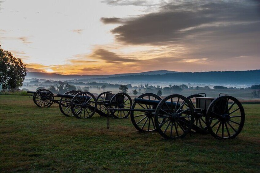 Una fila de cañones en un campo con un atardecer al fondo. 4