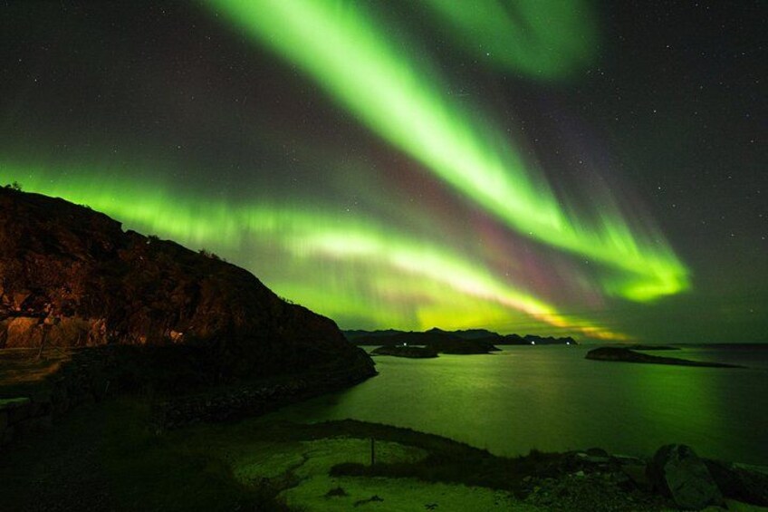 L'aurora boreale su un paesaggio costiero con un promontorio roccioso e acque calme. 5