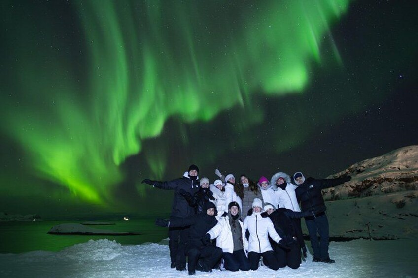 A group of people posing with the Northern Lights in a snowy landscape. 2
