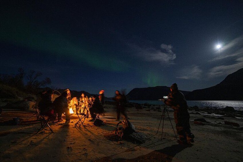 Un gruppo di persone attorno a un fuoco da campo di notte, mentre qualcuno scatta una foto. 3
