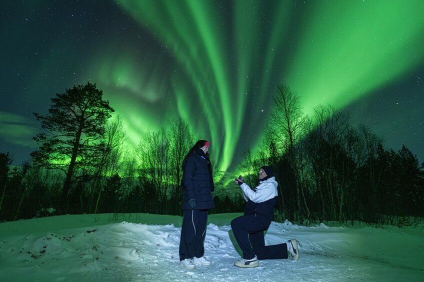 Una persona è inginocchiata sulla neve mentre un'altra è in piedi, sotto un cielo notturno illuminato dall'aurora boreale verde. 1