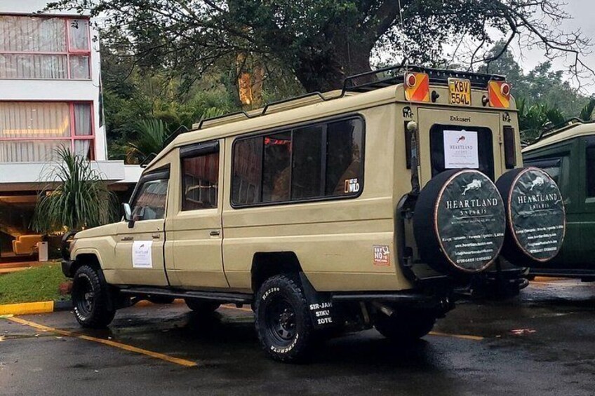 A beige off-road vehicle parked in a lot with a building and trees in the background. 2
