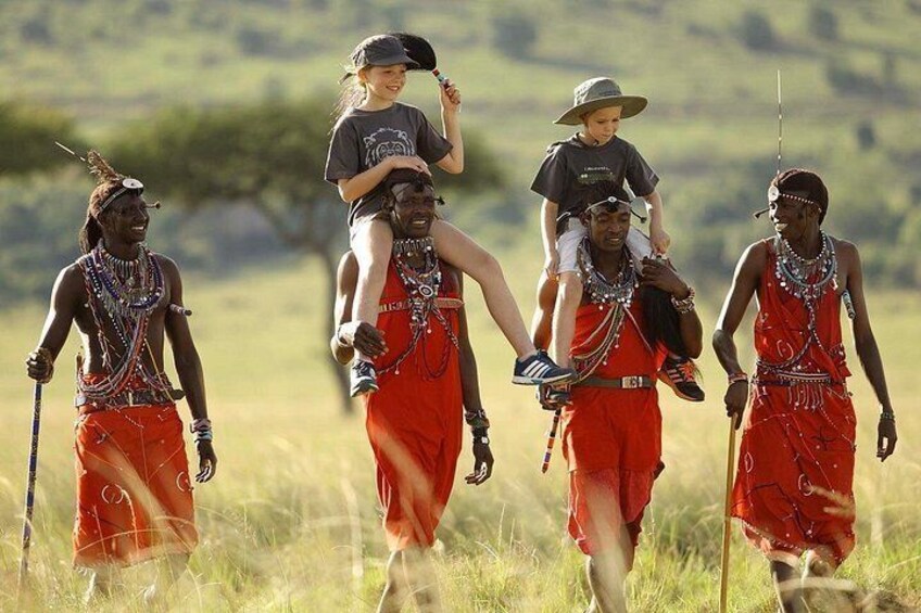 Maasai warriors in traditional attire walking through a grassy field. 4