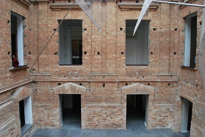 A brick building with multiple windows and doorways, some of which are open. 2